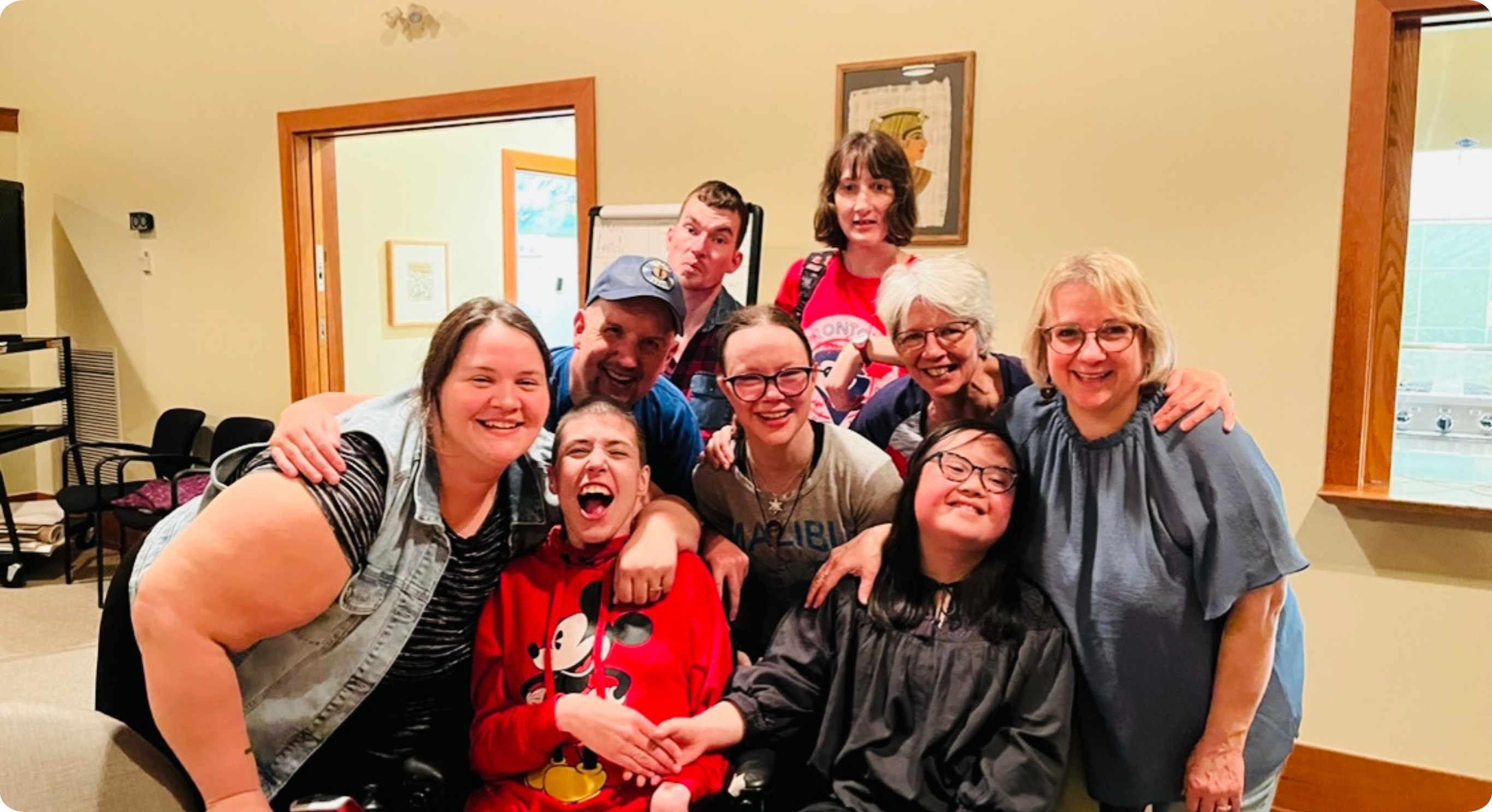 A diverse group of 9 people of various ages and ethnicities, with & without disabilities, posing for a photo at the 2022 in-person Youth Leadership training course.