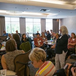 A diverse crowd of people sitting and listening to a woman standing with a microphone in the middle of the room at the Inclusive Housing Solutions Lab forum in New Brunswick.