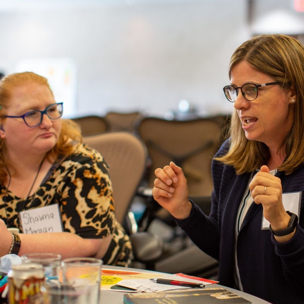 A young white woman with orange hair and glasses listening to a middle aged white woman with light hair and glasses at the Inclusive Housing Solutions Lab Forum in New Brunswick.