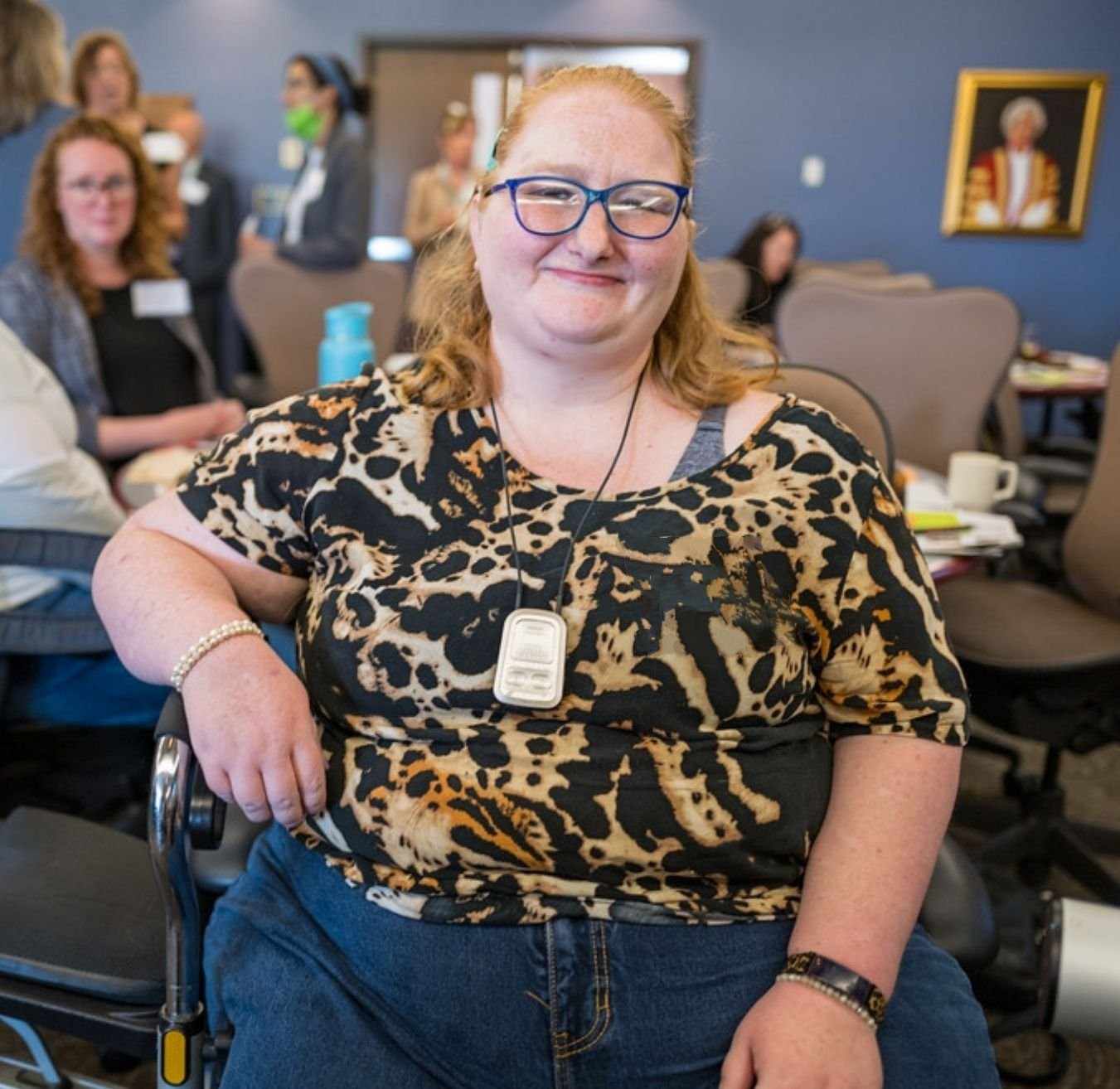 A white woman with orange hair and glasses sitting and smiling at the Inclusive Housing Solutions Lab Forum in New Brunswick.