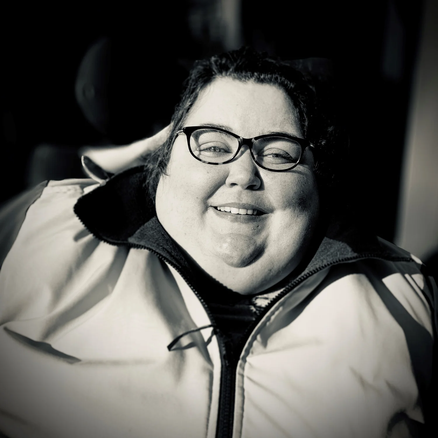 Black and white photograph a white woman with dark hair and glasses smiling.