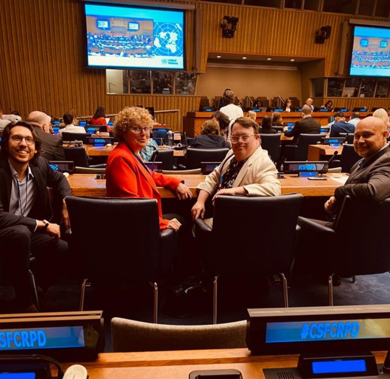 Jonathan Boulet-Groulx (L'Arche International), Lori Vaanholt, Nick Herd and Warren Pot (all from L'Arche Canada) looking behind them at the camera while seated at the 2023 Conference of the States Parties (COSP) at the UN in New York