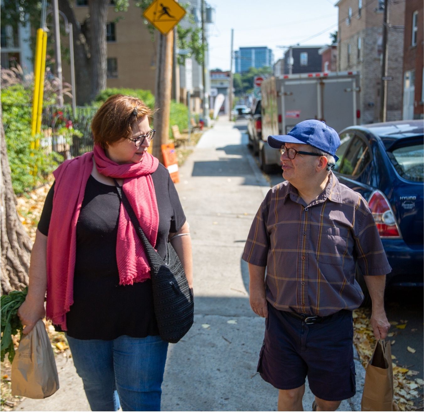Woman and a man walking down the street together holding paper bags looking at each other
